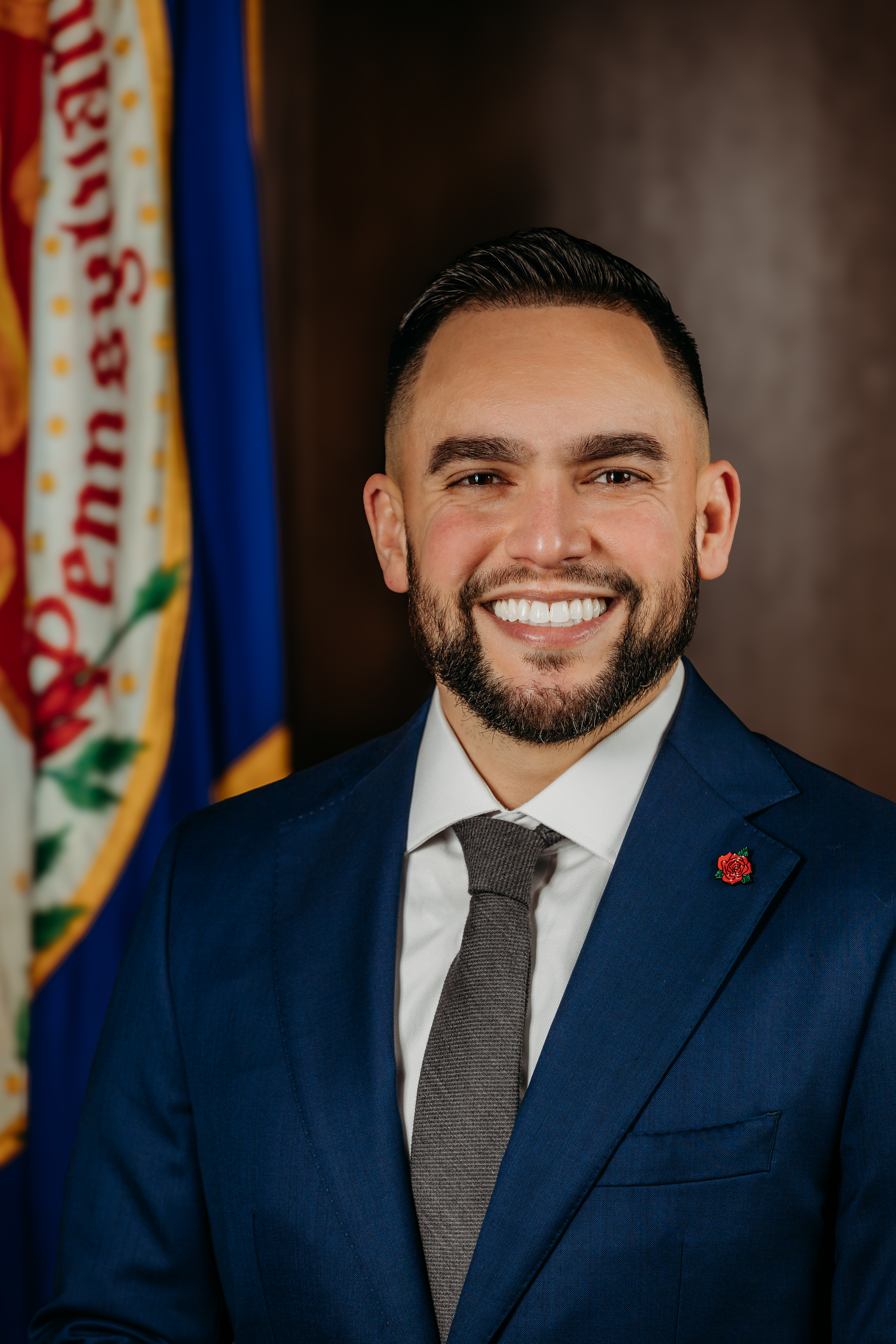 2026 Commencement Speaker Jaime Arroyo, Mayor of Lancaster Pennsylvania, posing in front of flag